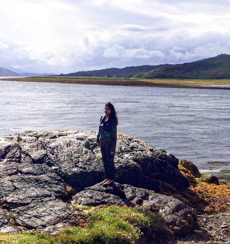 A girl standing on rocks with mountains and loch in the background