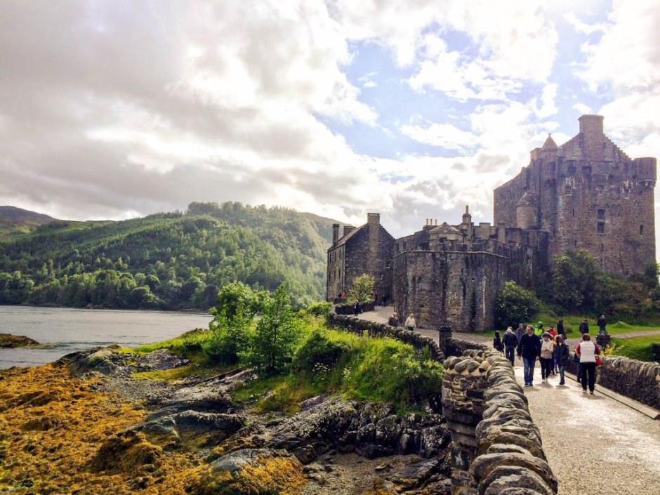 Eilean Donan Castle with mountains in the background and some people on the bridge connecting the castle with the mainland