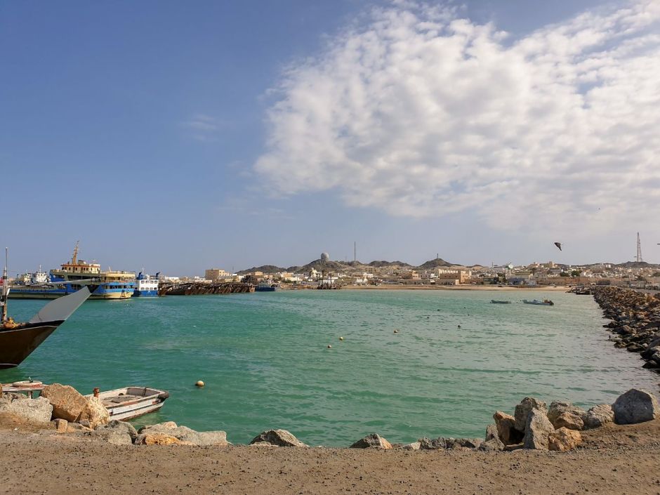Ferries parked at the port of Masirah Island with mountains and houses in the background